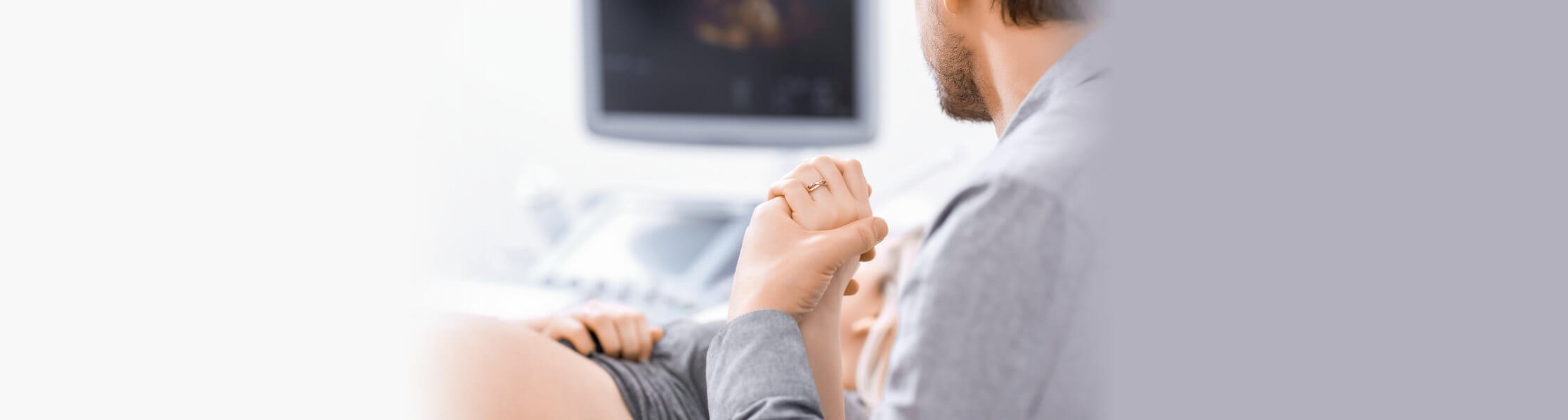woman laying on hospital bed with ultrasound monitor in background with man holding her hand