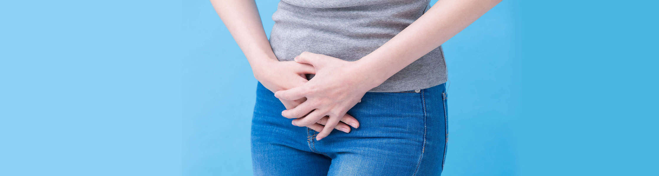 woman in jeans and t-shirt with hands crossed over her pelvic region