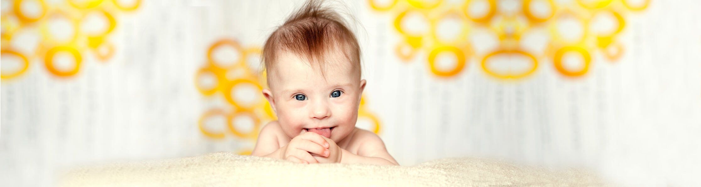 a happy baby laying face-forward propped on elbows looking at camera