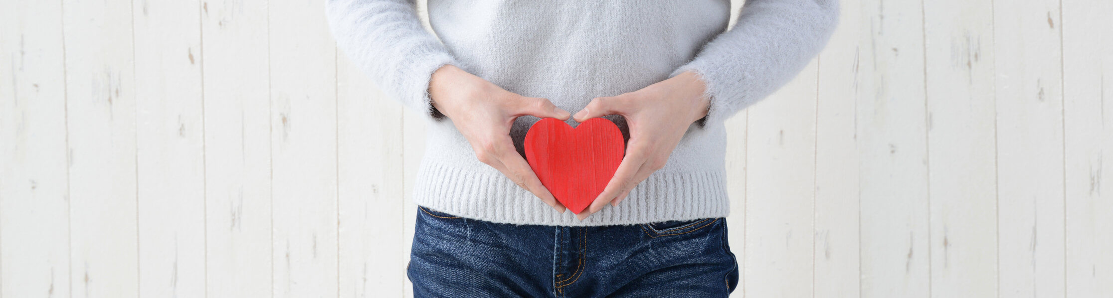 person holding a red heart shape with heart-shaped hands in front of their belly