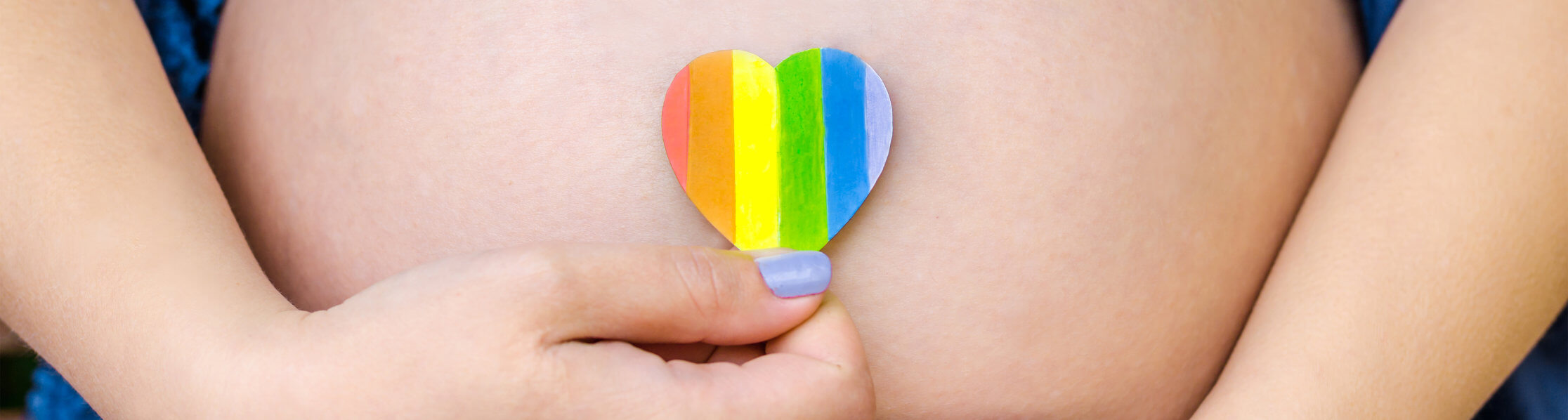 a female hand holding a rainbow heart over her belly